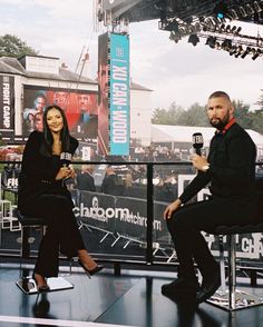 a man and woman sitting on chairs in front of a stage talking to each other