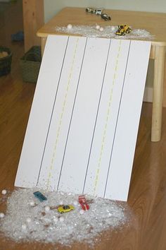 an easel sitting on top of a wooden floor filled with white sand and small toy cars