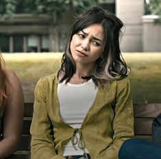 two women sitting on a bench with one looking at the camera and the other frowning