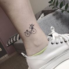 a small tattoo on the ankle of a woman's foot with a bicycle and flowers