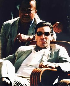 two men sitting next to each other with one wearing sunglasses and the other in a suit