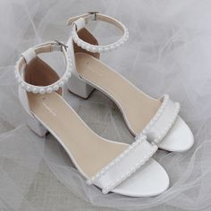 a pair of white high heeled shoes with pearls on the toe and ankle straps