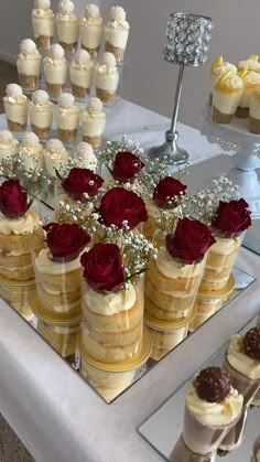 there are many desserts on the table with red roses in vases next to each other