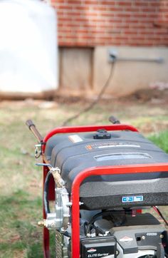 the back end of a small red and black engine on a lawn with grass in front of it