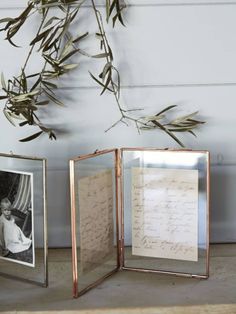 two silver frames sitting next to each other on top of a wooden floor with an olive branch