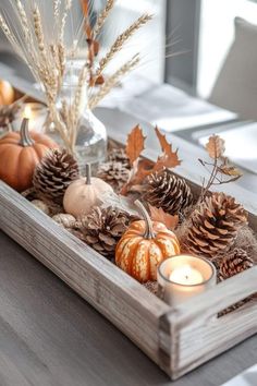 a wooden tray filled with pine cones, candles and other autumn decorations on top of a table