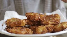 some fried food on a white plate and someone holding it in the background with their hands