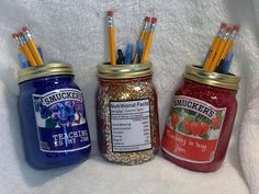 three jars with pencils in them sitting on a white blanket next to each other