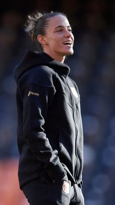 a female soccer player wearing a black hoodie and looking off to the side with her hands on her hips