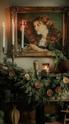 a mantle with candles and greenery in front of a painting on the wall above it