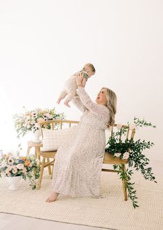 a woman holding a baby in her arms while sitting on a chair with flowers and greenery