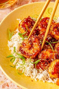 a yellow plate topped with rice and shrimp next to chopsticks on top of it