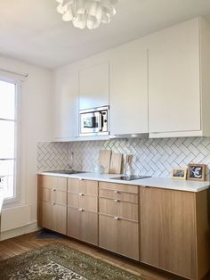 a kitchen with white cabinets and wood flooring next to a window in an apartment