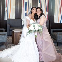 two brides pose for a photo in front of the lobby at their wedding reception