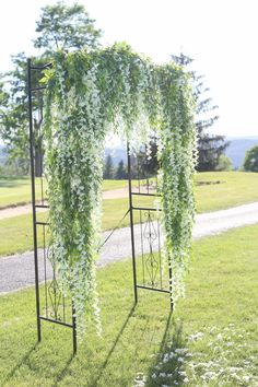 an outdoor wedding ceremony with white flowers and greenery hanging from the top of it