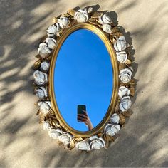 a hand holding a cell phone in front of a round mirror with shells on it