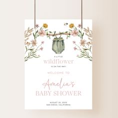 a baby shower sign hanging from a rope with flowers and leaves on it's side