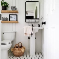 a white toilet sitting next to a sink in a bathroom under a mirror and shelves