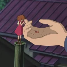 a hand holding onto a small doll on top of a wooden pole in front of a purple roof