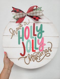 a hand holding up a wooden sign that says merry holiy jolly christmas on it