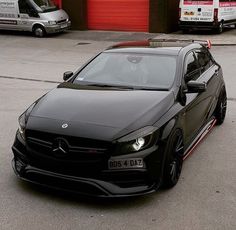 a black mercedes cla parked in front of a red garage with two vans behind it