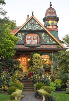 a green house with lots of plants and bushes around it's front door, surrounded by greenery