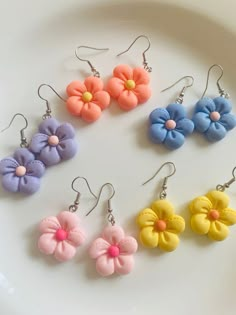 six different colored flower earrings sitting on top of a white plate