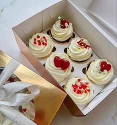 a box filled with lots of cupcakes covered in white frosting and red hearts