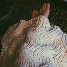 someone is laying down on the ground with their feet propped up in a knitted blanket