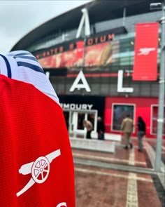 the back of a person's red jersey in front of a large stadium building