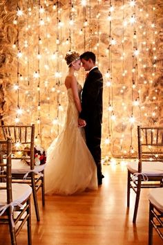 a bride and groom are standing in front of a backdrop with lights on the wall