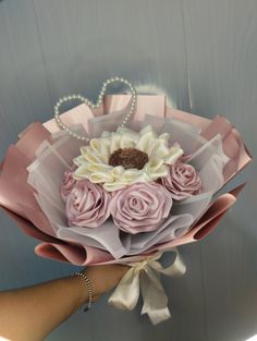 a person holding a bouquet of flowers with pearls on the end and pink ribbon around it