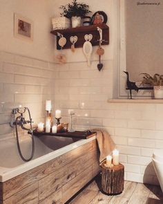 a bath tub sitting next to a wooden shelf filled with candles and potted plants