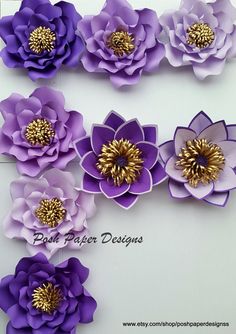 purple and gold paper flowers are arranged on a white board