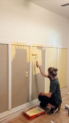 a woman is painting the walls with yellow paint and she is sitting on the floor