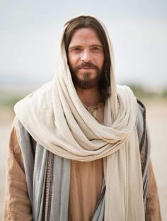 jesus with long hair and beard wearing a beige shawl over his head, looking at the camera