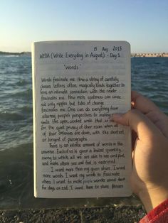 someone is holding up a book with writing on it in front of the water and sky