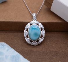 Adorn yourself with the ethereal beauty of nature embodied in our Silver Flower Pendant. This exquisite piece features a captivating oval Larimar stone nestled within an intricately crafted silver frame, reminiscent of a blooming flower in full splendor. Oval Larimar Center Stone: At the heart of this enchanting pendant lies a mesmerizing oval Larimar stone, exuding the serene blue hues and captivating patterns characteristic of this rare gem. The stone serves as the focal point, drawing the eye with its natural allure. Oval Silver Frame with Cut-Out Triangle Shapes: Surrounding the oval Larimar stone is a delicate silver frame meticulously fashioned into the shape of a flower. The frame is adorned with charming cut-out triangle shapes, enhancing the pendant's floral motif and adding depth Teardrop Larimar Jewelry Gift, Oval Blue Larimar Jewelry, Gift Necklaces With Oval Cabochon Natural Stones, Oval Cabochon Necklaces With Natural Stones For Gifts, Larimar Cabochon Jewelry Gift, Round Larimar Jewelry Gift, Round Larimar Jewelry For Gifts, Oval Cabochon Natural Stone Jewelry Gift, Oval Larimar Jewelry For Anniversary