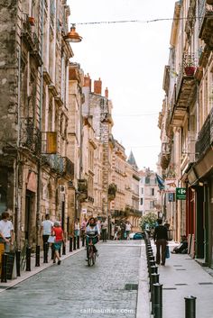 people are walking and riding bicycles down the street in an old european city with stone buildings