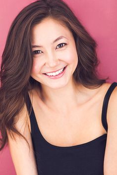 a woman with long brown hair smiling at the camera while wearing a black tank top