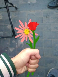 a person holding up a flower with a smiley face on it