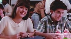 two young people sitting at a table with food and drinks in front of them,