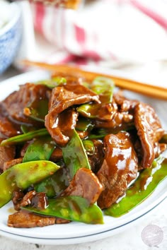 a white plate topped with stir fry beef and green peppers next to chopsticks