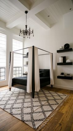 a canopy bed sitting on top of a wooden floor next to a white and black rug