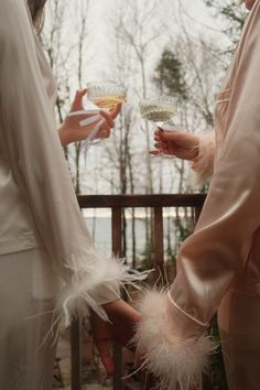 two women dressed in white holding wine glasses with feathers on them, and one wearing a pink dress