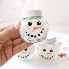 a hand holding a glass jar with a snowman in it and another one behind it