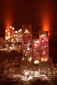 the centerpieces are filled with pink flowers and lit candles in glass vases