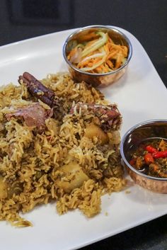 a white plate topped with rice and meat next to bowls of sauces on a table