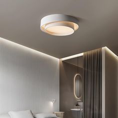 a white bed sitting under a round light next to a mirror on the side of a wall