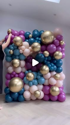 a woman standing in front of a giant balloon arch with gold and blue balloons on it